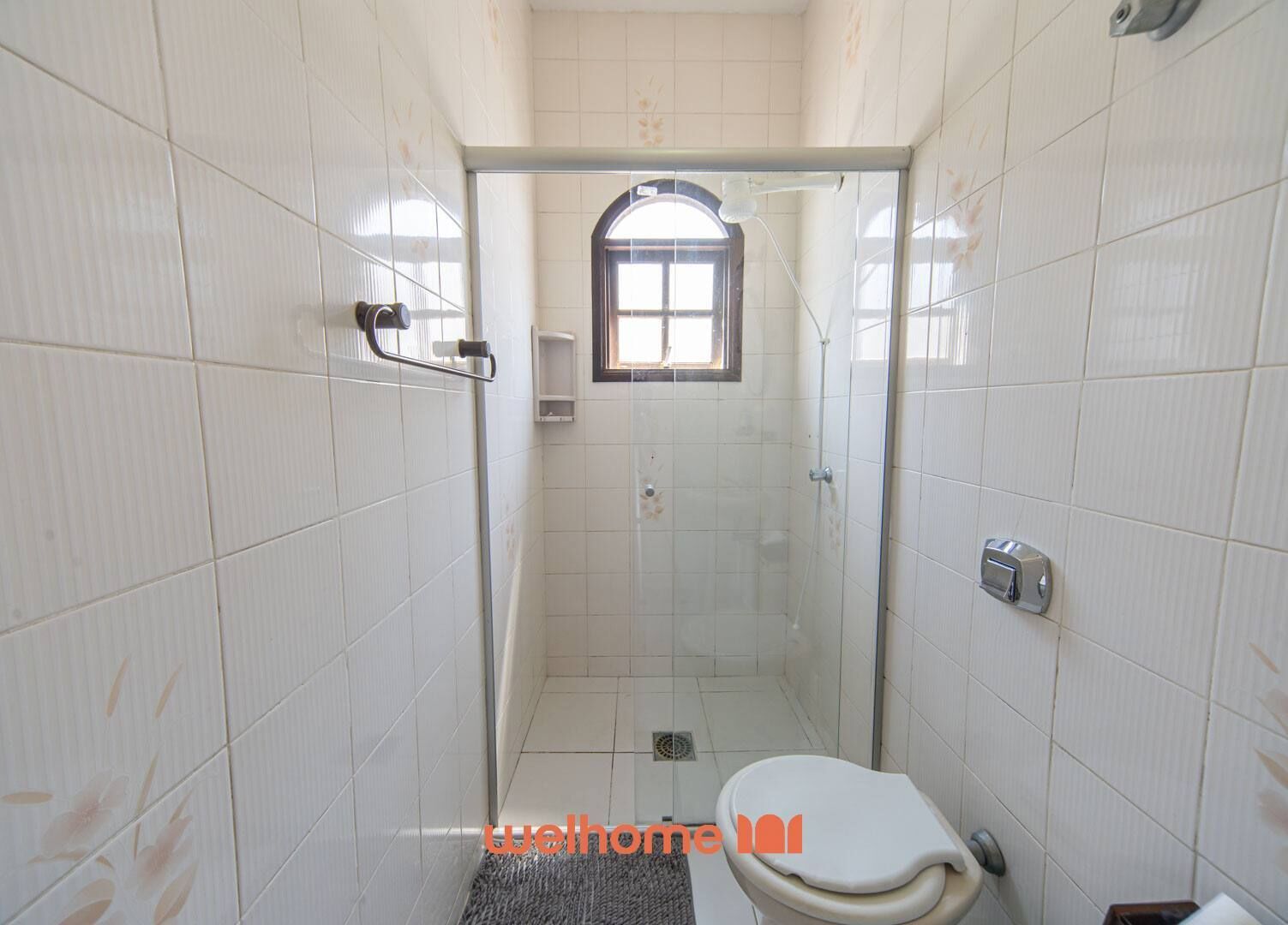 A small, tiled bathroom with a shower, a toilet, and a window.