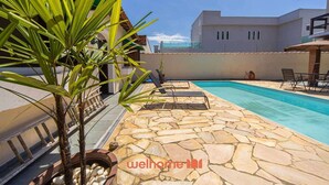 A swimming pool with stone tiles, lounge chairs, and a palm tree.