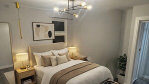 Ett modernt sovrum med en stor säng, sängbord, en hängande lampa och en spegel.