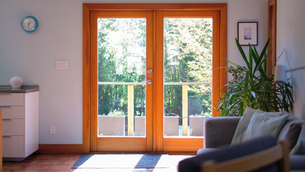Una habitació amb una porta corredissa de vidre que dona a un balcó, un sofà, una planta i un rellotge a la paret.