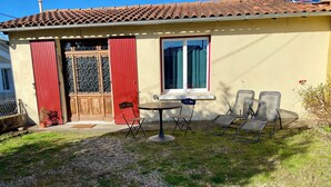Una casa con techo de tejas, una puerta roja y un pequeño patio con una mesa y dos sillas.