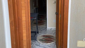 Una puerta de madera que da a una habitación con un tapete estampado y una mesa de comedor con sillas.
