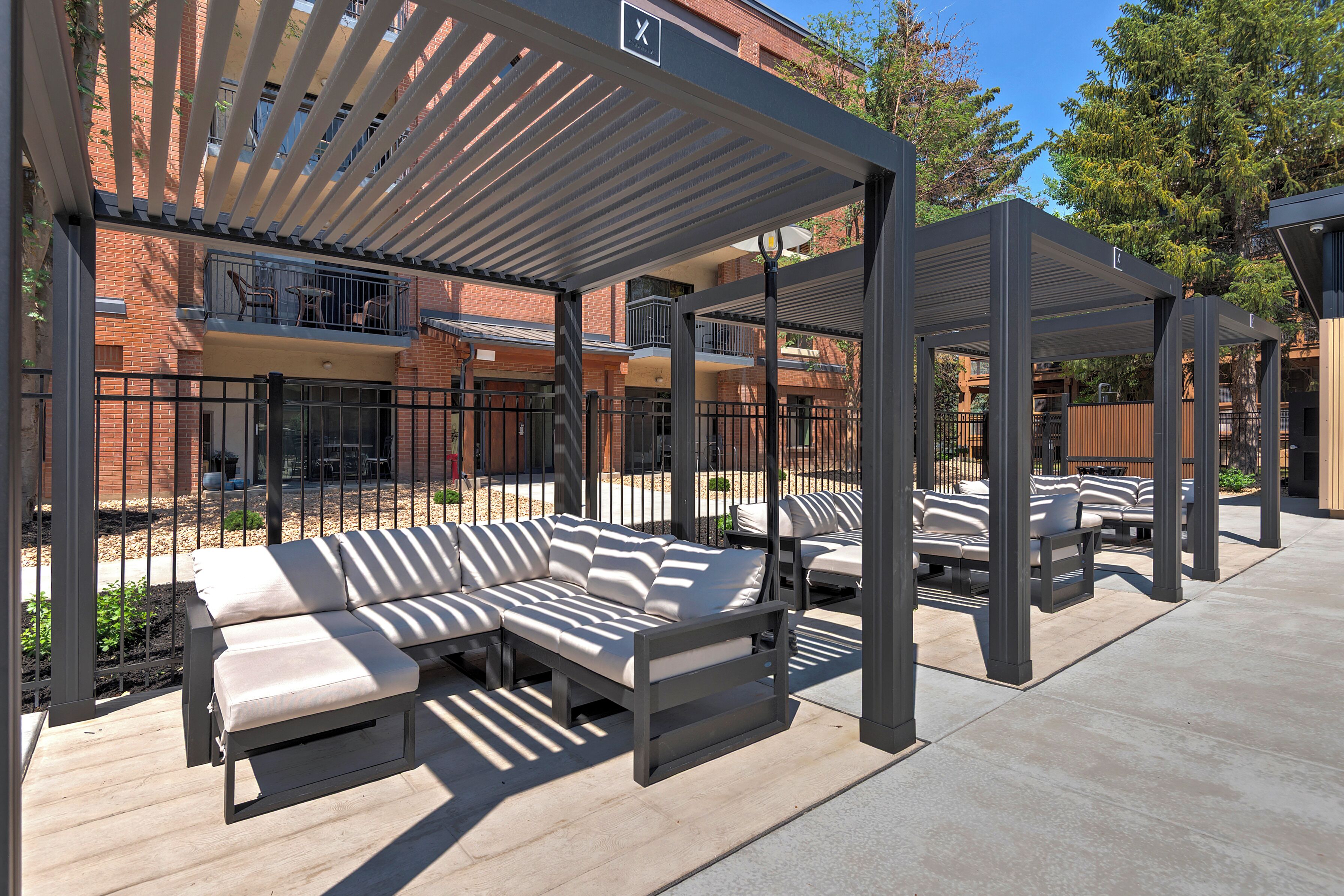 Un área de estar exterior con una pérgola cubierta, un sofá modular y una silla de lounge.
