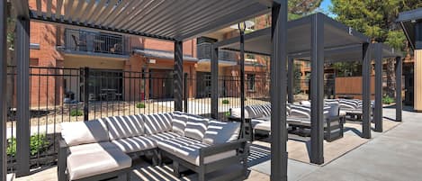 Un área de estar exterior con una pérgola cubierta, un sofá modular y una silla de lounge.