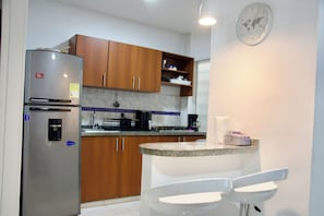 A kitchen with wooden cabinets, a stainless steel refrigerator, a granite countertop, and a white sink.