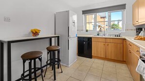Eine kleine Küche mit Kühlschrank, Geschirrspüler, Holzschränken, einem Fenster mit Blick und zwei Barhocker.