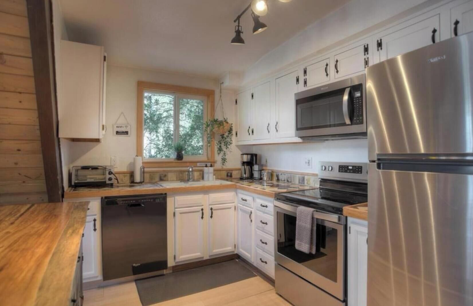 A modern kitchen with white cabinetry, stainless steel appliances, and a large window providing natural light.