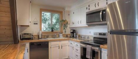 A modern kitchen with white cabinetry, stainless steel appliances, and a large window providing natural light.