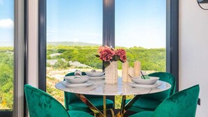 A dining area with a table set for four, green upholstered chairs, a vase with pink flowers, and candles. - Luxury apartment LaRiv II with pool (Krk)