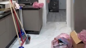En smal hall med ett köksutrymme på ena sidan, där det finns ett kylskåp, en tvättmaskin och diverse rengöringsmedel.