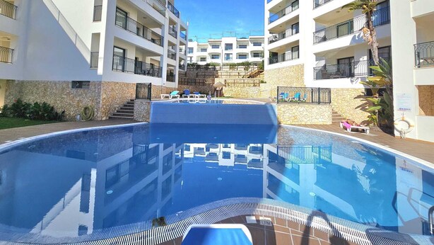 Un hotel moderno con piscina centrale, numerosi balconi e facciata in pietra.