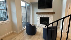 Amplia sala de estar con chimenea, un ventanal grande y una escalera.