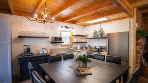 A modern kitchen with wooden beams, a chandelier, and a dining area with a welcome mat.