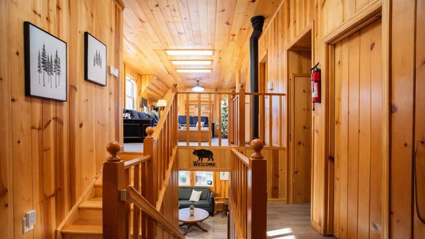 A wooden interior with a staircase leading to a lower level. There are framed pictures on the walls, a welcome sign with a bear, and a fire extinguisher mounted on the wall.
