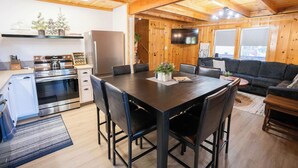 A modern kitchen with a dining area, wooden ceiling, and a flat-screen TV.