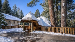A wooden gazebo with a snow-covered roof, surrounded by a wooden fence and snow-covered ground.