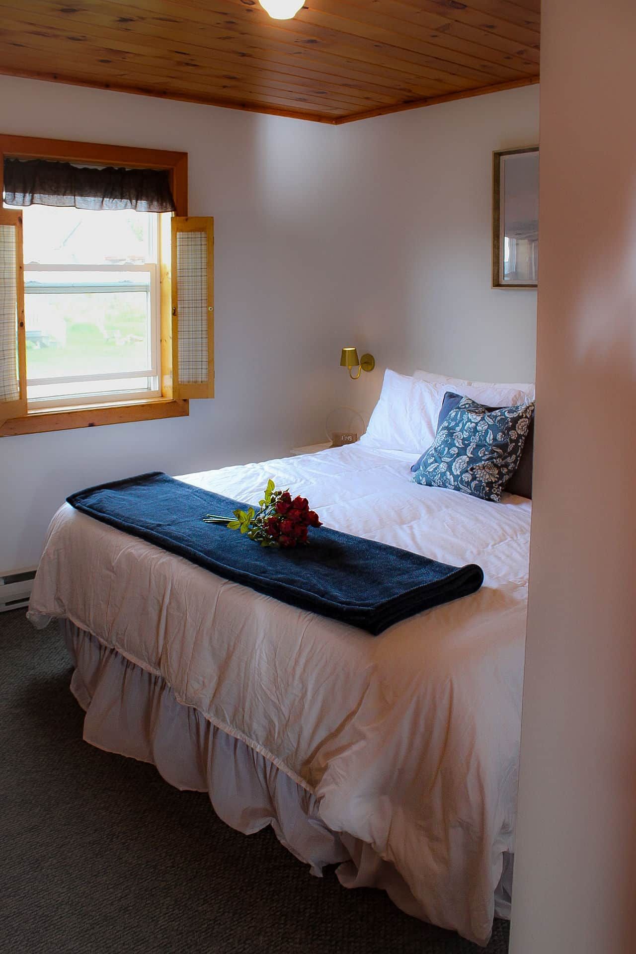 A bedroom with a bed, a window, a wall-mounted lamp, and a framed picture.