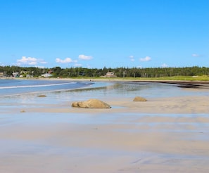 A beach with clear skies, calm waters, and a few rocks in the foreground.