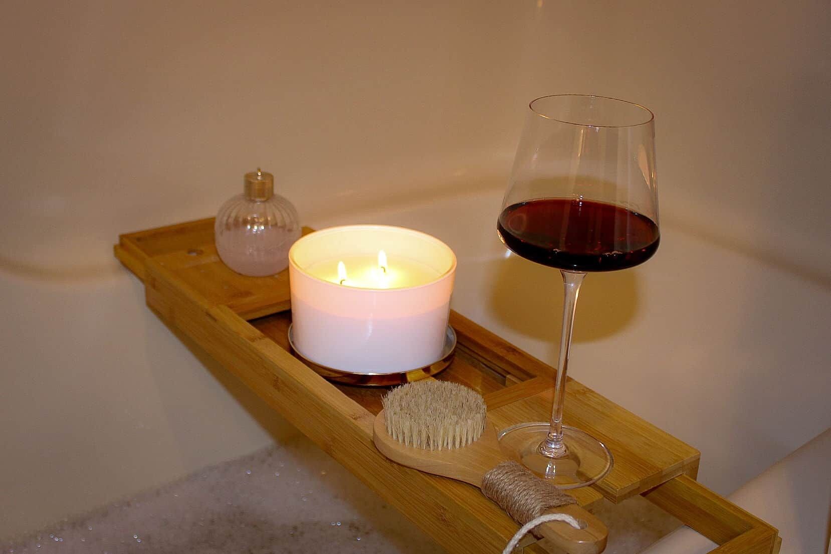Et stearinlys, et glas rødvin og en træbakke på et bord.