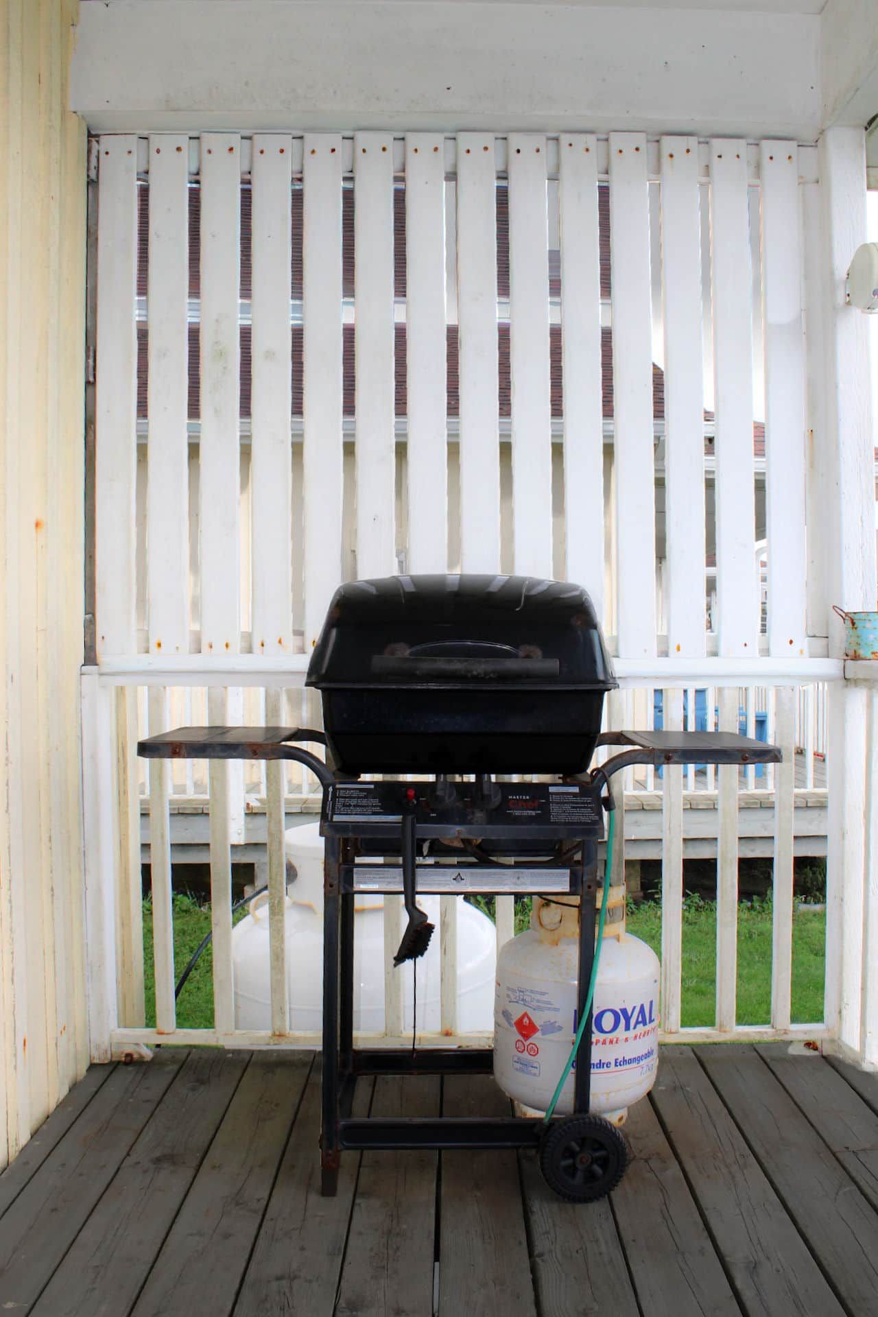 A barbecue grill on a wooden deck with a white fence in the background.