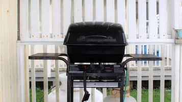 A barbecue grill on a wooden deck with a white fence in the background.
