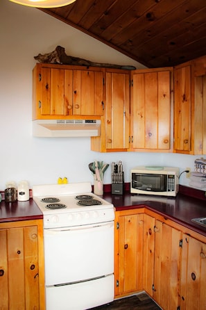 Una cocina con armarios de madera, una estufa blanca, un microondas y diversos utensilios de cocina.