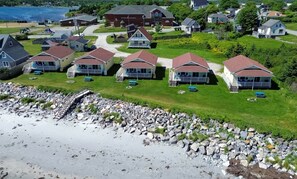 A coastal residential area with houses featuring gabled roofs and front porches, a rocky shoreline, and a clear view of the water.
