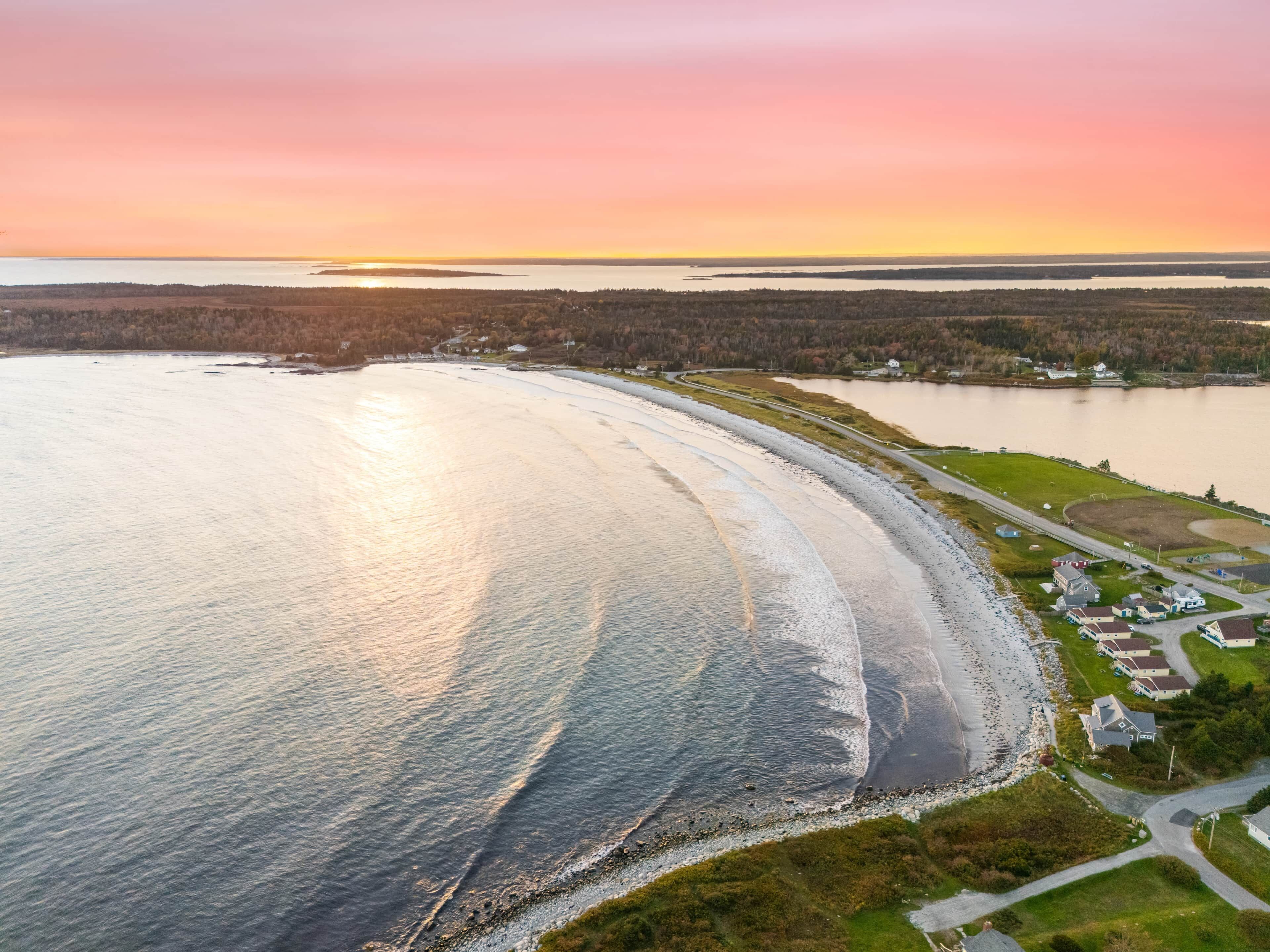 An aerial view of a coastal area with a beach, a road, and residential buildings.