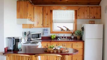 Eine Küche mit Holzausbau, einem Esstisch mit zwei Stühlen, einem Kühlschrank und einem Fenster mit Jalousien.