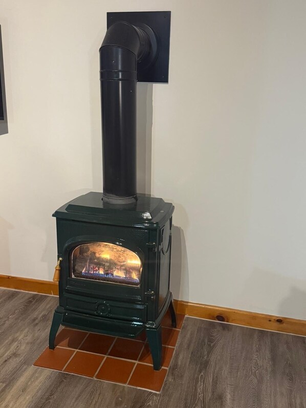 A green wood-burning stove with a chimney, placed on a tiled floor against a white wall.