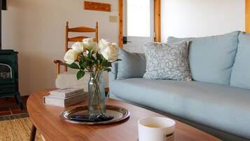 A wooden table with a vase of white flowers, a remote control, a book, and a candle.