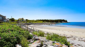 A coastal beach with a wooden walkway, houses, and a rocky shoreline.