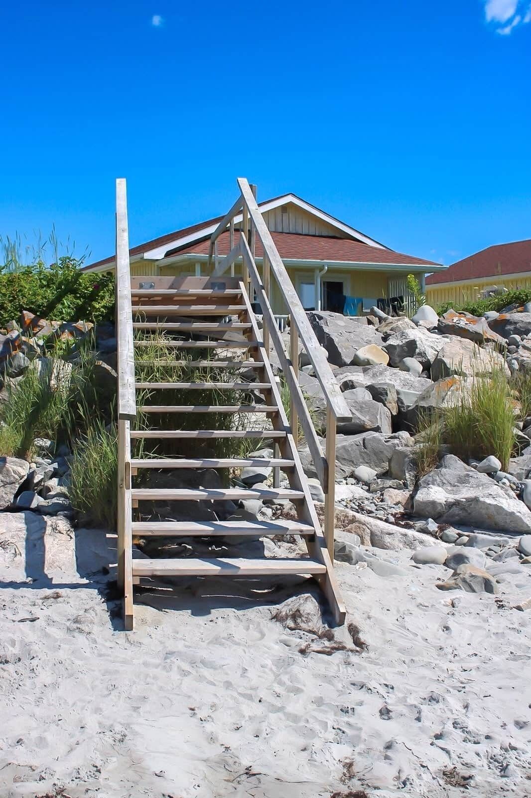 A wooden staircase leading to a building with a red roof, surrounded by rocks and sparse vegetation.