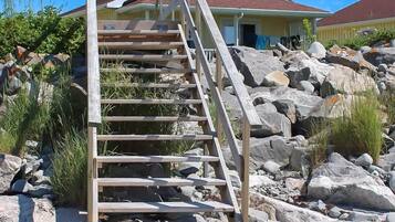 A wooden staircase leading to a building with a red roof, surrounded by rocks and sparse vegetation.