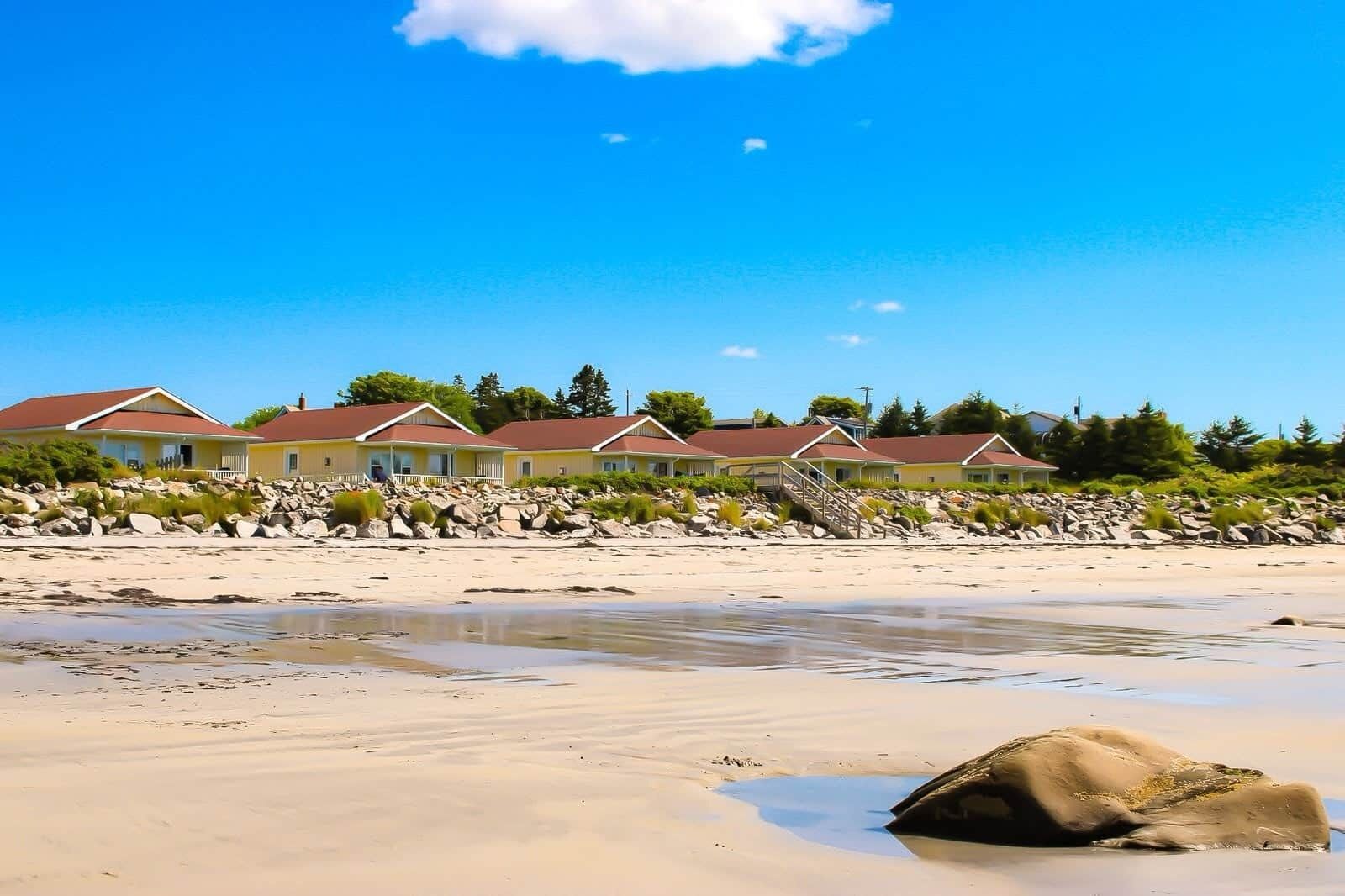 A beachfront property with multiple houses, a sandy beach, and a rocky shoreline.