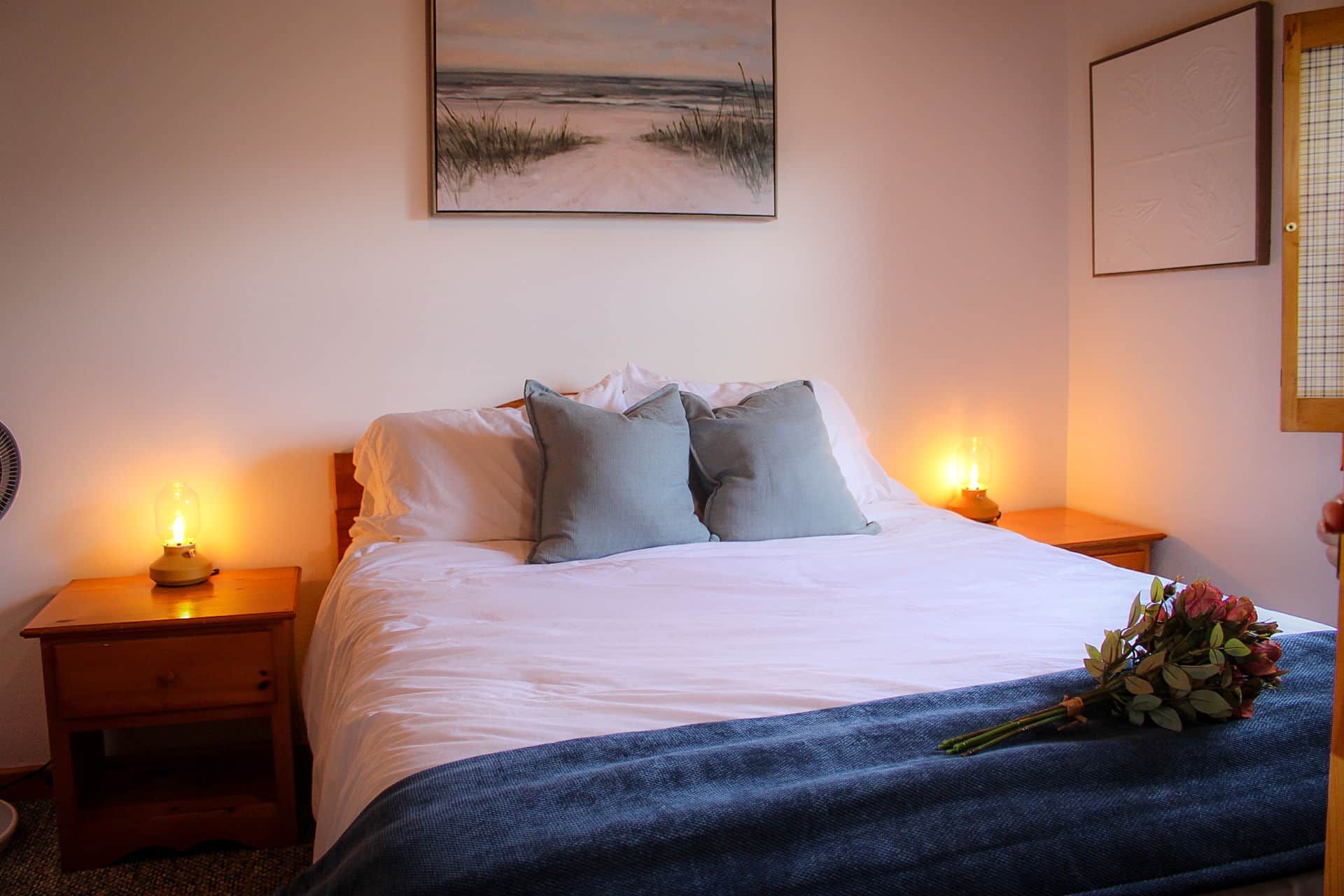 A bedroom with a bed, bedside lamps, a wall-mounted picture, and a bedside table with a lamp.