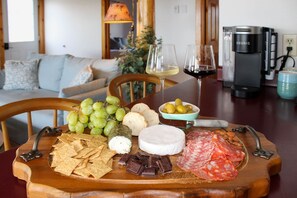 Taula de fusta amb aperitius, formatge i embutits, amb una màquina de cafè i un sofà al fons.