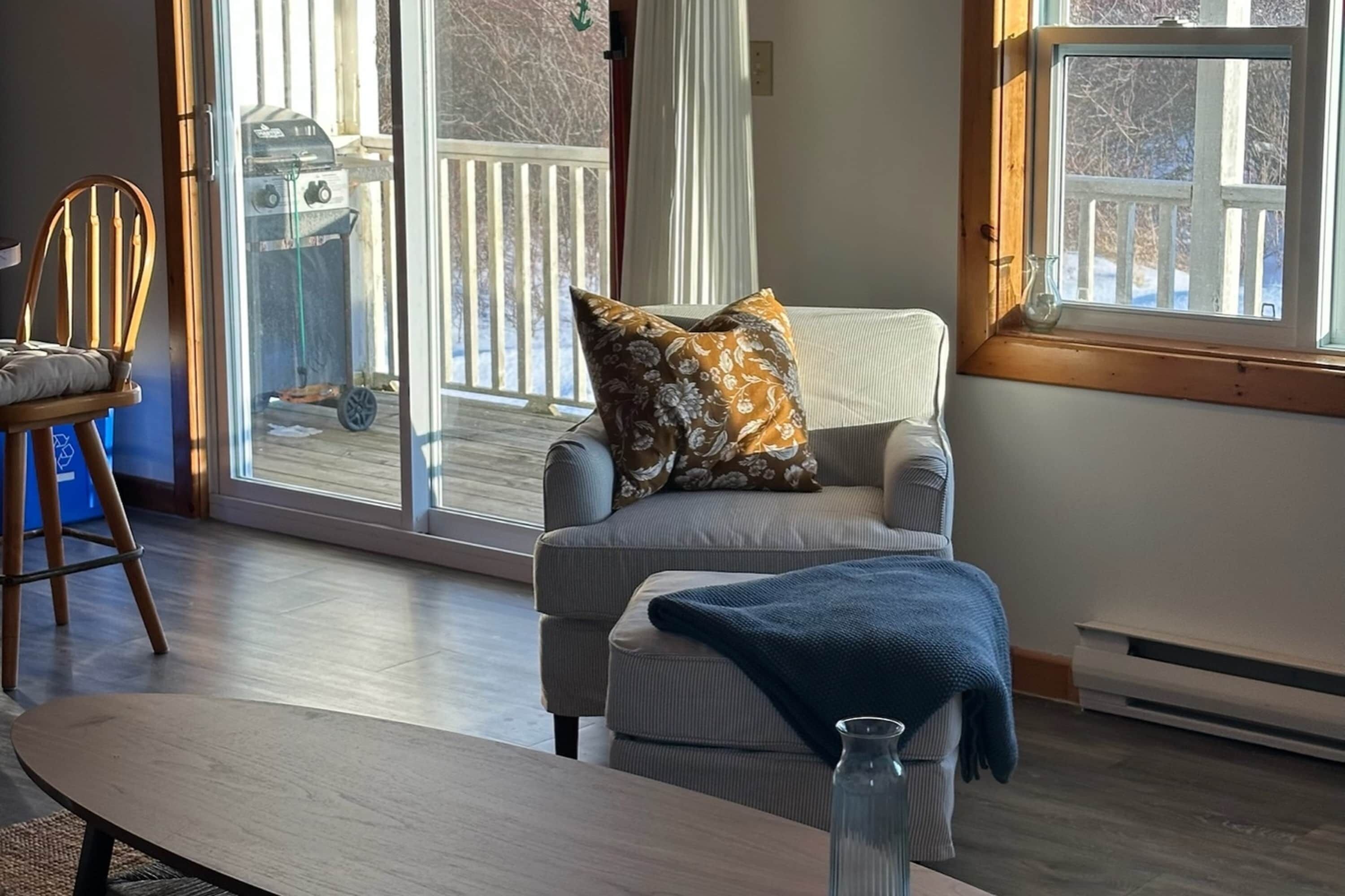 A cozy living room with a grey armchair, a wooden chair, and a small table.