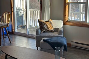 A cozy living room with a grey armchair, a wooden chair, and a small table. - Oceanfront 2-Bedroom Cottage | King Bed | Pet-Friendly Getaway (Lockeport)