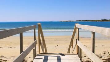 A wooden boardwalk leading to a beach with clear blue water and a distant shoreline.