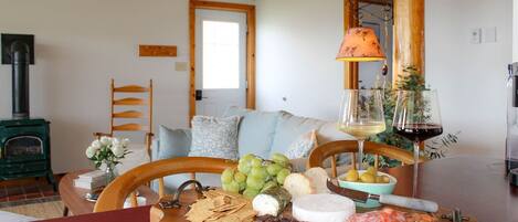 Una habitación acogedora con techo de madera, chimenea, una mesa de comedor con una tabla de quesos y una lámpara.
