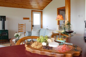 A cozy room with a wooden ceiling, a fireplace, a dining table with a cheese board, and a lamp.