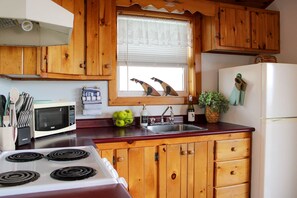 Une cuisine avec des meubles en bois, un four à micro-ondes, une cuisinière, un évier et une fenêtre agrémentée d’objets décoratifs.