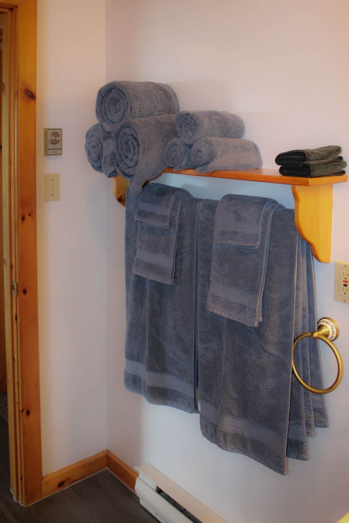 Ein Badezimmer mit Handtuchhalter, der gerollte und gefaltete Handtücher trägt, einer Holztür und einem an der Wand befestigten Lichtschalter.