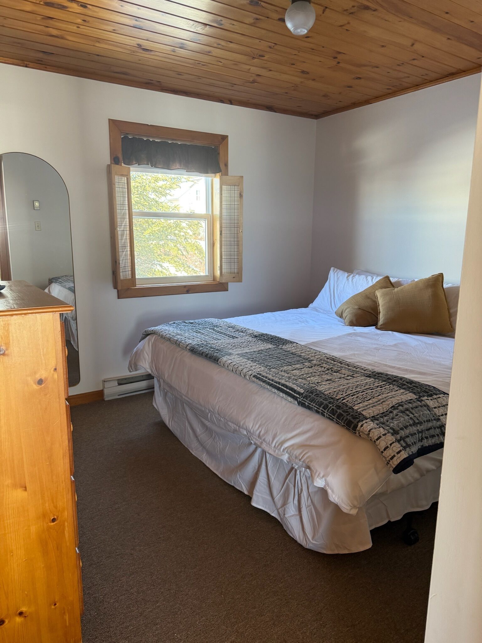 Ein Schlafzimmer mit Bett, einem Fenster mit Blick, einer Holzkommode und einem Deckenventilator.