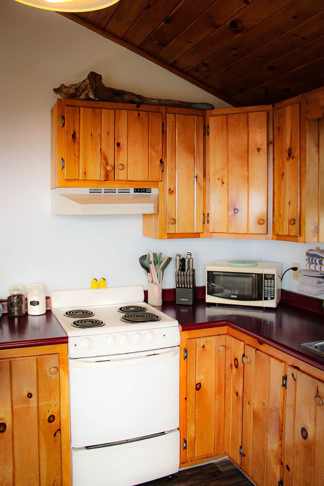 A kitchen with wooden cabinets, a white stove, a microwave, and various kitchen utensils.
