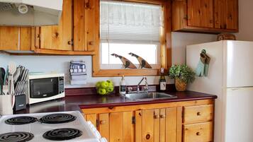 Une cuisine avec des meubles en bois, un four à micro-ondes, une cuisinière, un évier et une fenêtre agrémentée d’objets décoratifs.