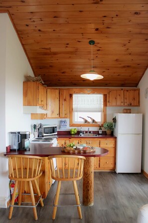 A kitchen with wooden cabinets, a dining table with two chairs, a refrigerator, and a window with blinds.