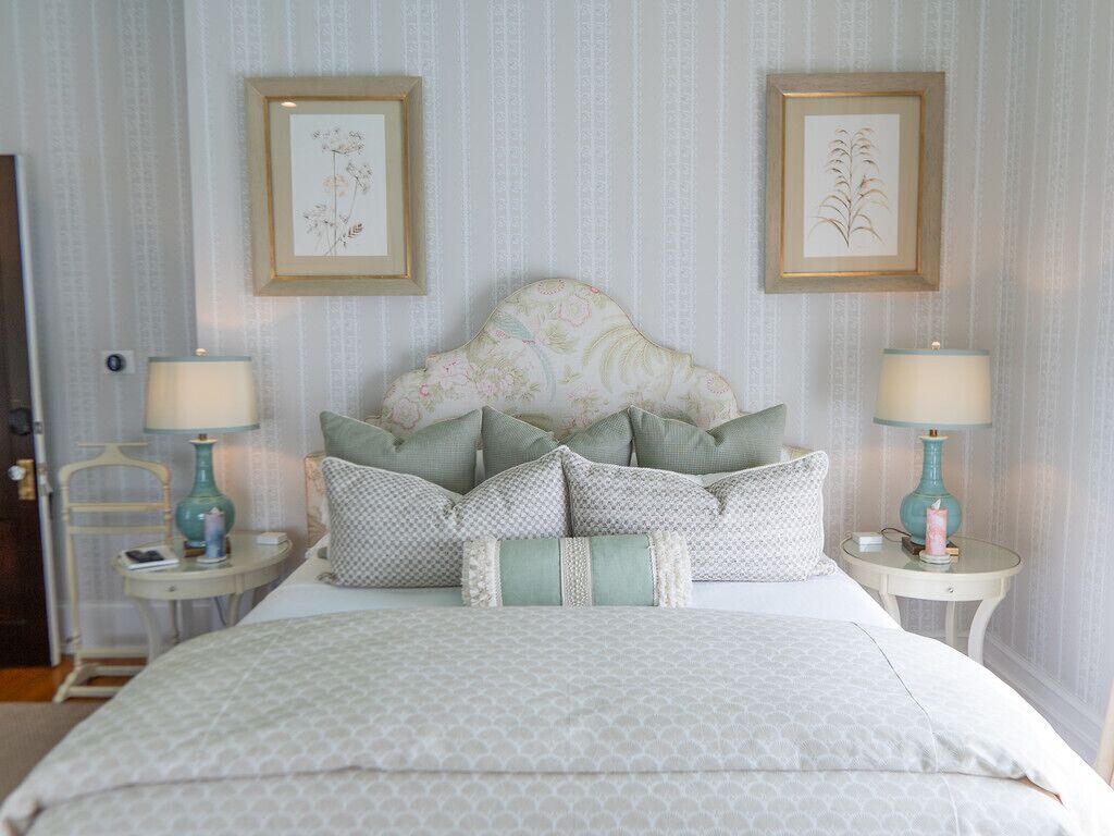 Een keurig opgemaakt slaapkamer met een groot bed, twee nachtkastjes met lampen, en twee ingelijste botanische prints aan de muur.