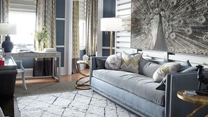 A modern living room with a grey sofa, a large peacock painting, and a dining area with a white table and chairs. - Pandora's Manor Bed & Breakfast (High Point)
